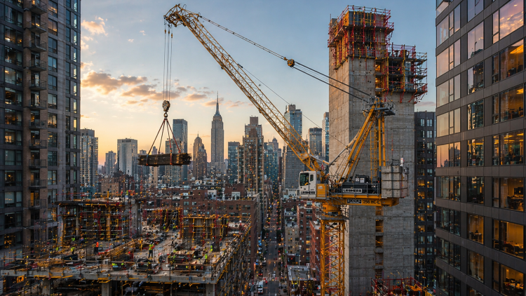 A luffing jib tower crane operating between buildings on a dense urban construction project - construction cranes